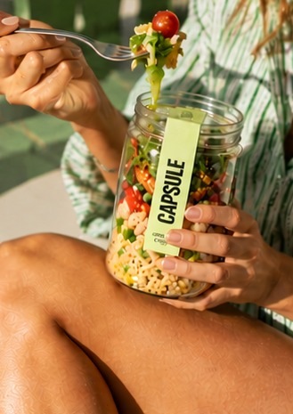 Someone lifting a fork of salad from a Capsule jar outdoors